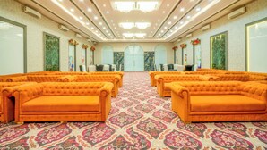 Un salón de conferencias con filas de sofás naranjas, alfombra estampada y una lámpara de araña.