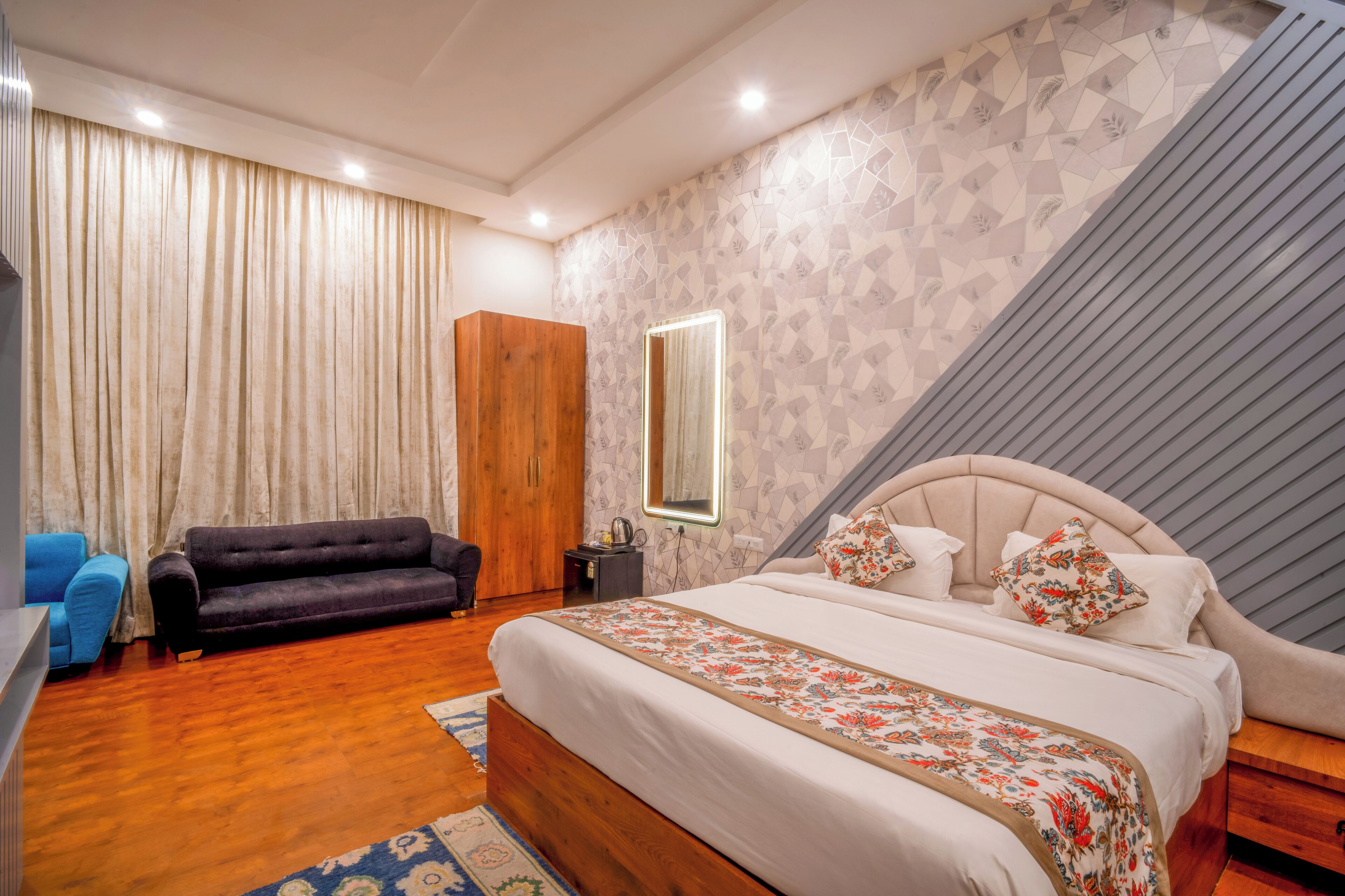 A bedroom with a large bed, a wooden wardrobe, a blue sofa, and a mirror on the wall.