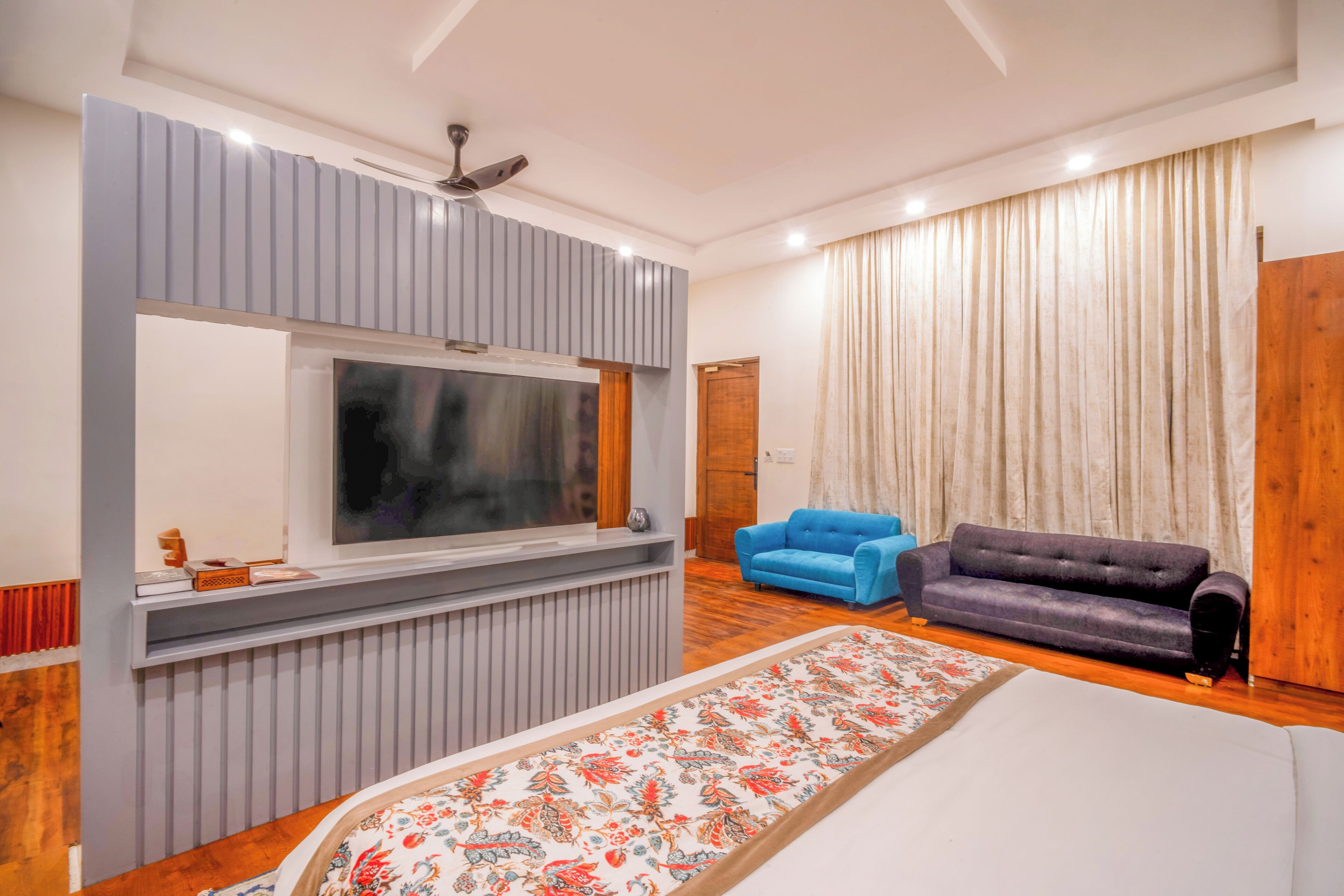 Un dormitorio moderno con una cama grande, un televisor montado en la pared, un sofá azul y un armario de madera.