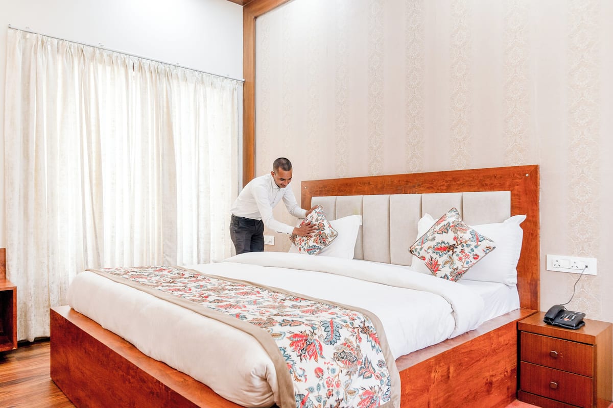 A neatly made bed with a floral bedspread, a wooden headboard, and a bedside table with a phone.