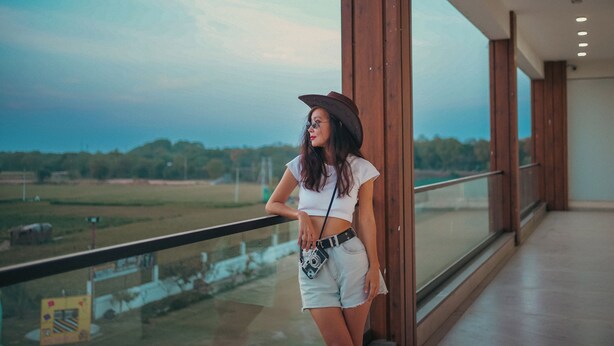 Una mujer de pie junto a una barandilla de vidrio con vistas a un campo y árboles a lo lejos.