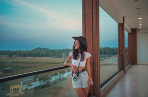 A woman standing by a glass railing with a view of a field and trees in the distance.