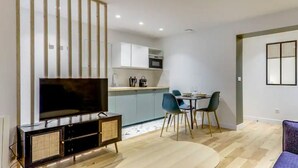 Ein modernes Wohnzimmer mit Flachbildfernseher, einem Essbereich mit blauen Stühlen und einer Küche mit weißen Schränken.