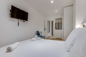 Een moderne hotelkamer met een groot bed, een flatscreen televisie aan de muur, een blauwe stoel en een raam met uitzicht op de gang.