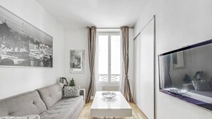 A modern living room with a grey sofa, a white coffee table, and a large window with curtains. - The Vendôme - Elegant&Business by Mon Petit Faré (Paris)
