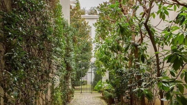 A narrow, paved pathway flanked by lush greenery and a metal gate, leading to a building. - Hidden beauty - low cost -courtyard -Best location (Paris)
