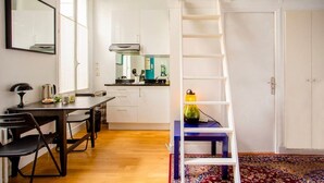 A compact room with a bunk bed, a desk with chairs, a kitchen area, and a patterned rug. - Hidden beauty - low cost -courtyard -Best location (Paris)