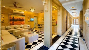Un lobby de hotel lujoso con piso a cuadros, un conjunto de sofás, una araña y un cuadro grande de una escena desértica.