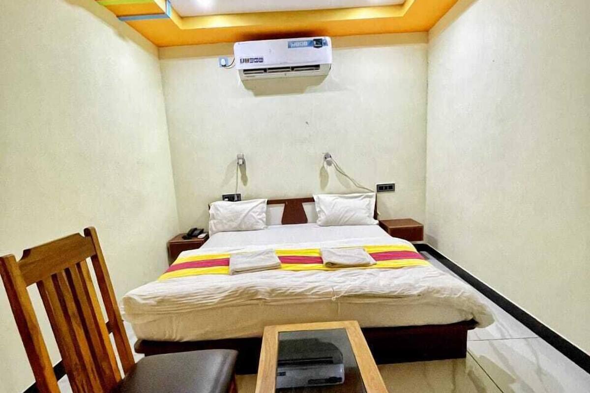 Ein kleiner, gut beleuchteter Raum mit einem Bett, einem Sessel, einem Tisch und einem Deckenventilator.