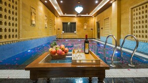 Un área de spa con piscina, una mesa de madera con frutas y vasos, y una botella de vino Sula.