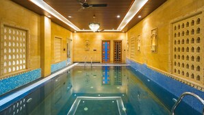 Una piscina con techo de madera, paredes enlosadas y un candelabro.