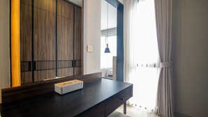 A modern bedroom with a dark wooden dresser, a bedside table with a tissue box, and a large window with curtains. - De Kunyit Villa (Tabanan)