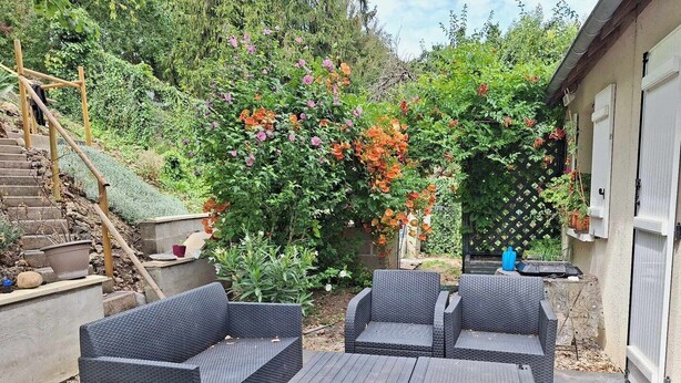 Een terras met rieten meubilair, een stenen trap en diverse planten en bloemen.