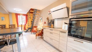 Een moderne keuken met een ingebouwde oven, een eethoek met een tafel en stoelen, en een trap naar een hoger gelegen verdieping.