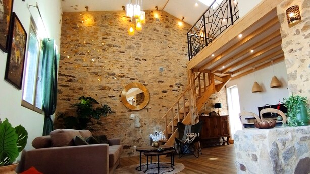 Amplia sala de estar con pared de piedra, escalera de madera y muebles modernos.