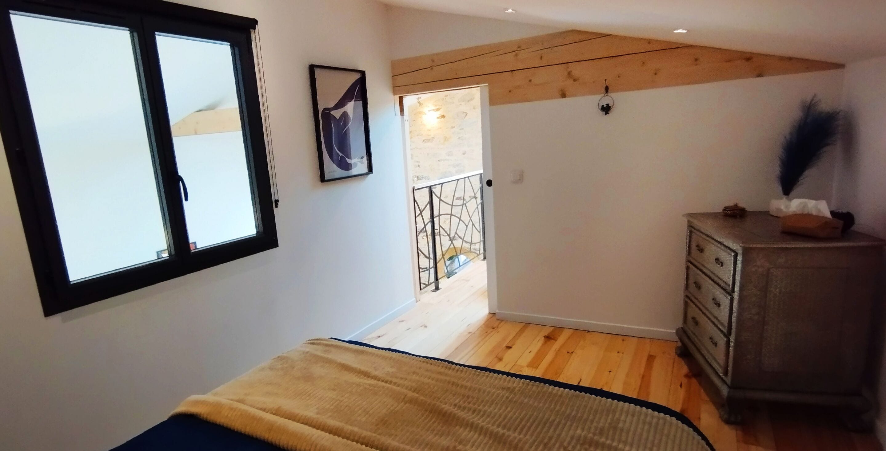 A bedroom with a bed, a dresser, a window, and a door leading to a balcony.