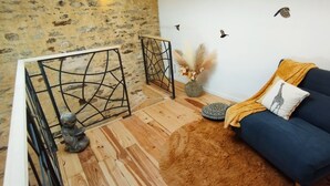 Una sala de estar acogedora con un sofá azul, una reja de metal decorativa, suelo de madera y pared de piedra.