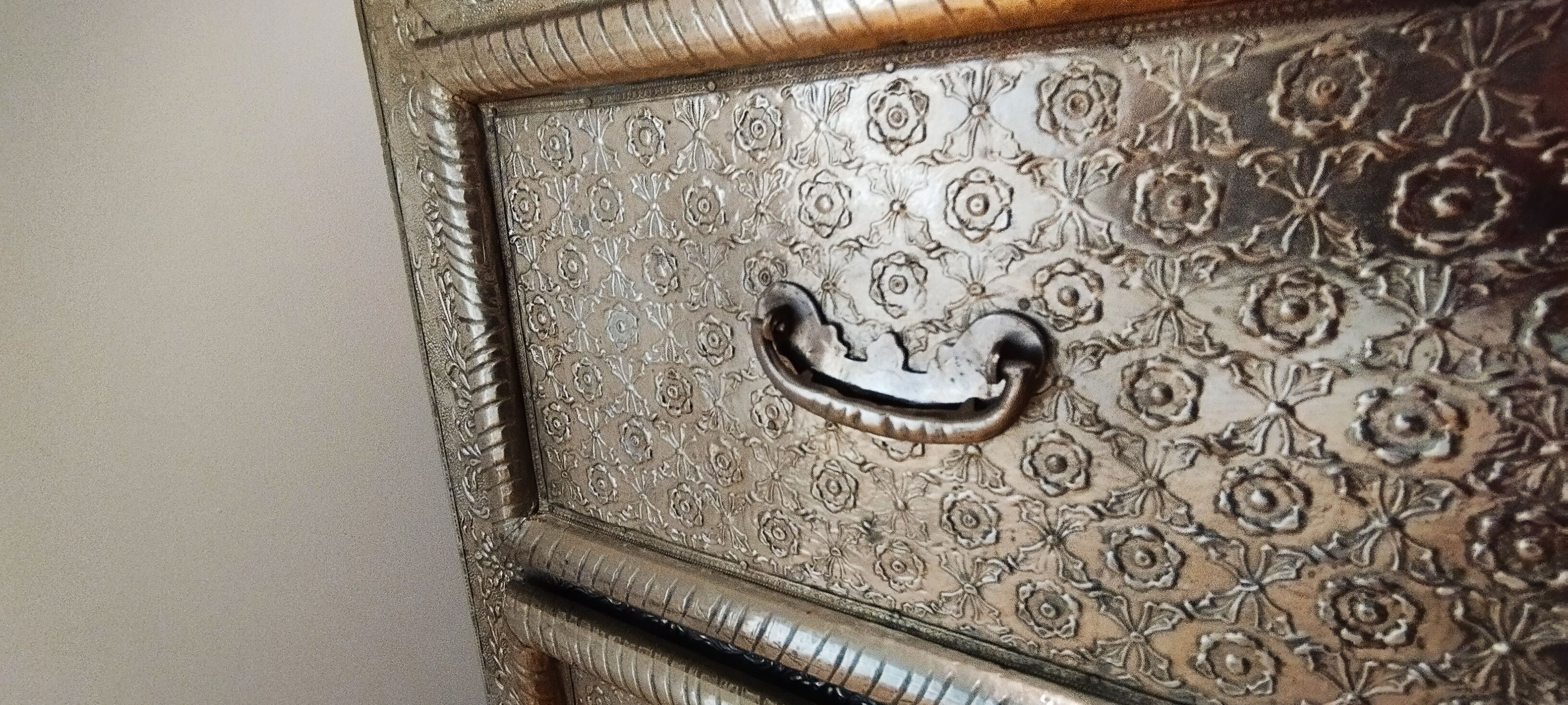 Un mobile metallico con motivo floreale e maniglia curva.