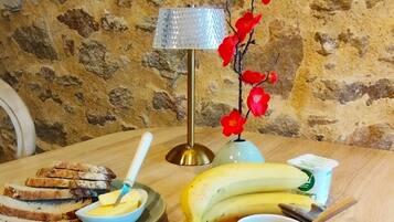 A breakfast setting with bread, banana, orange juice, coffee, and condiments on a wooden table against a stone wall.