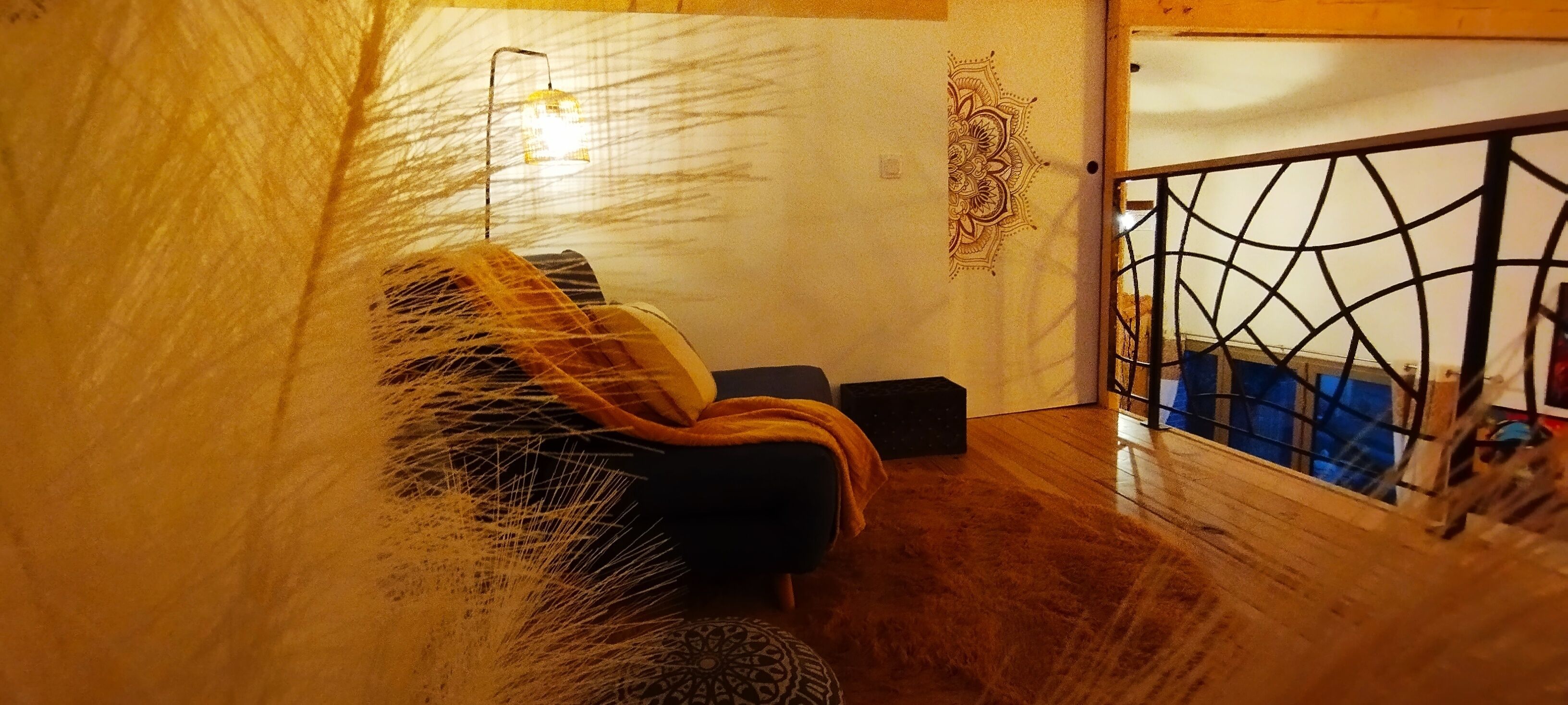 A room with a wooden floor, a black chair, a patterned rug, a wall with a decorative design, and a metal gate.