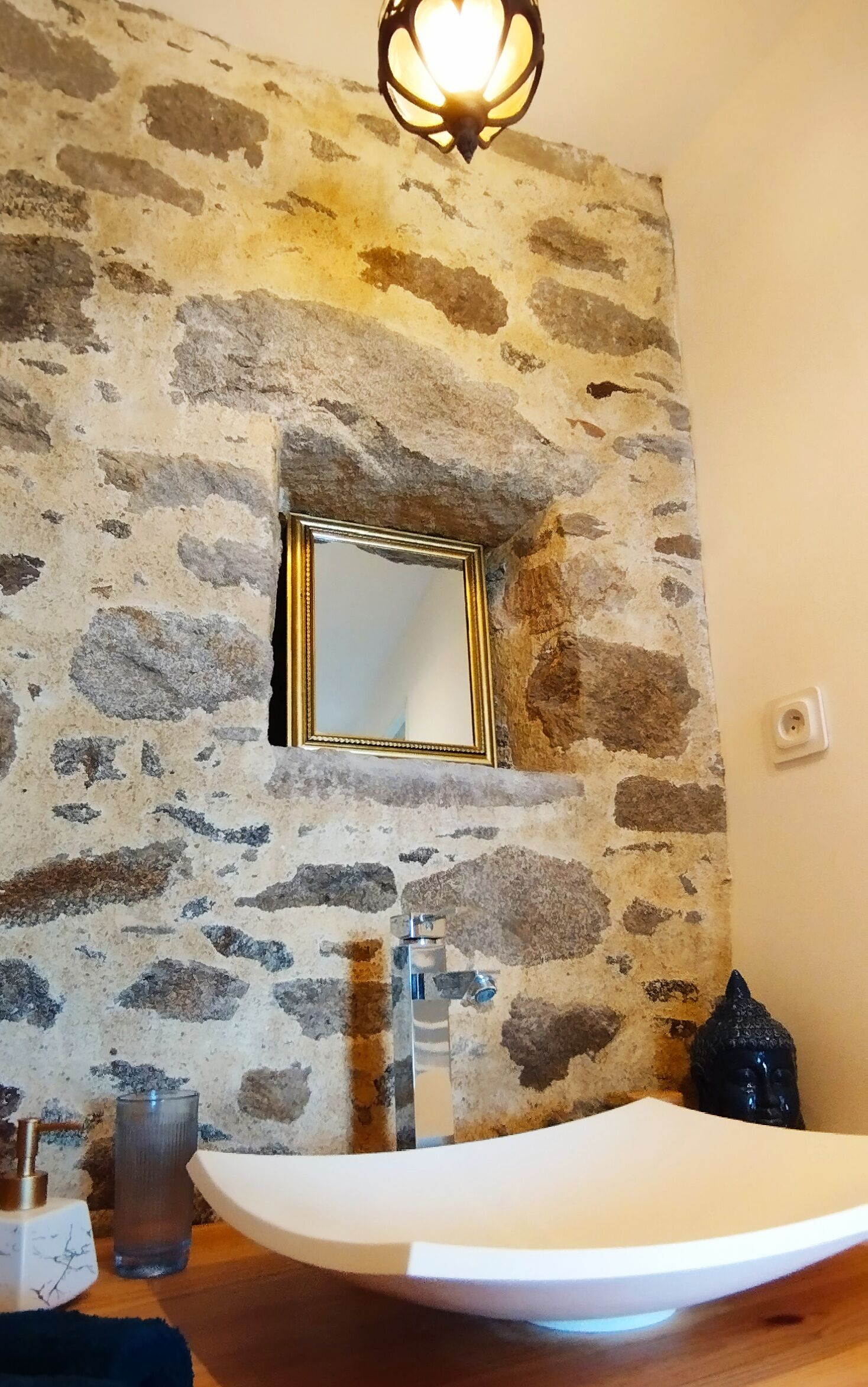 A bathroom with a stone wall, a mirror, a sink, and a Buddha statue.