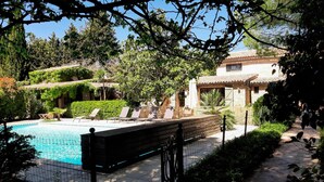 A pool area with lounge chairs and a stone wall. - Charming stone house with airco and a large pool (Lorgues)