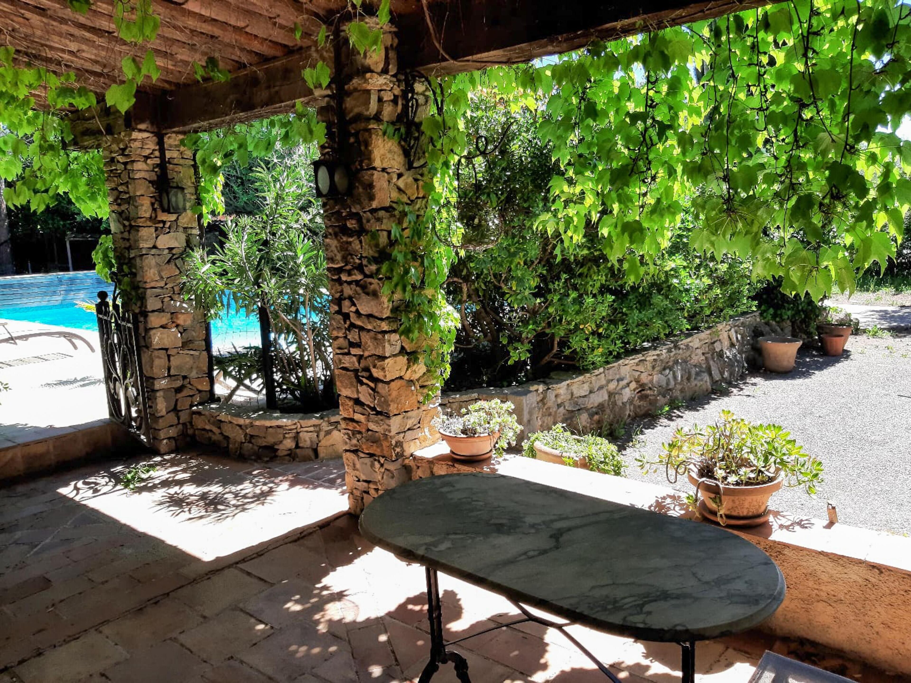 A covered patio area with stone pillars, potted plants, and a view of a swimming pool.