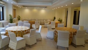 A conference room with round tables and white chairs, featuring a ceiling with recessed lighting and a large window on the left. - Hotel Forest Avenue (Dehradun)