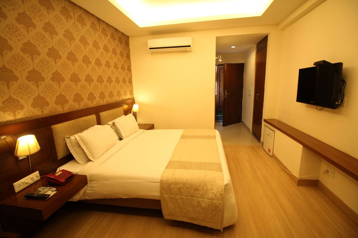 A hotel room with a large bed, bedside lamps, a TV, and an air conditioning unit.