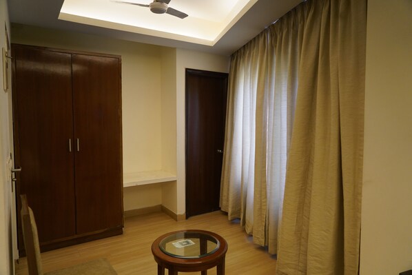 A room with a ceiling fan, a wooden wardrobe, a door, and a glass table.