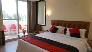 A hotel room with a large bed, a wooden headboard, a small table with a vase of flowers, and a balcony with red chairs. - Hotel Forest Avenue (Dehradun)