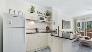 A modern kitchen with white cabinets, a built-in microwave, and a coffee maker. There is a small island with a sink and a seating area with a sofa and a coffee table.