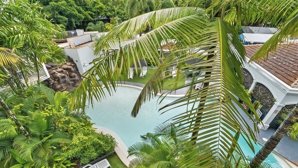 A pool surrounded by lush greenery and white lounge chairs.