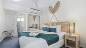 A neatly made bed with a teal accent, a bedside lamp, and a mirror on the wall.