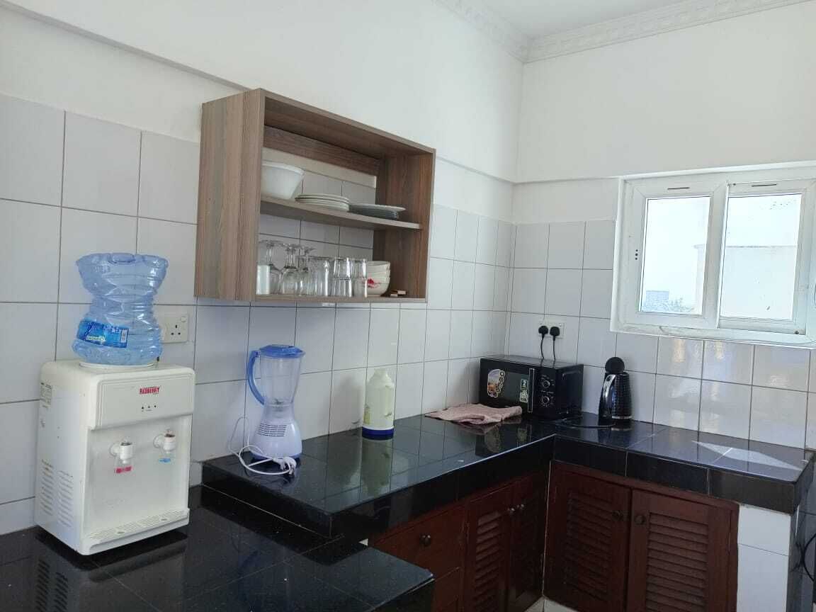 A kitchen with a water dispenser, blender, microwave, and wooden cabinets.
