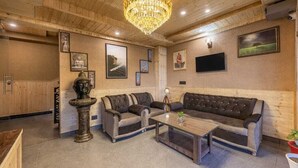 Een knus vertrek met een houten plafond, een kroonluchter, een zithoek, een salontafel en wanddecoratie.