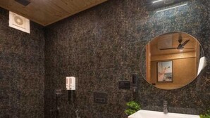Een moderne badkamer met een houten plafond, donkere stenen wanden, een ronde spiegel, een witte wastafel en een toilet.