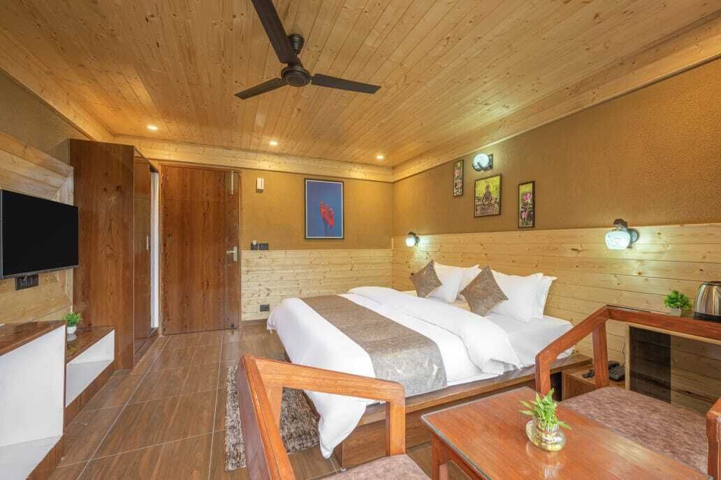 A hotel room with a wooden ceiling, a bed with white bedding, a television, and a small table with a plant.