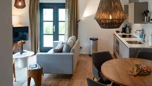 A modern living room with a sofa, a dining table with chairs, a TV, and a kitchen area with a sink and cabinets. - Skylgerduin (Midsland)