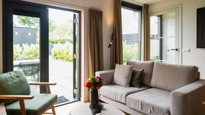 A modern living room with a sofa, a chair, a coffee table, and a vase of flowers. - Skylgerduin (Midsland)