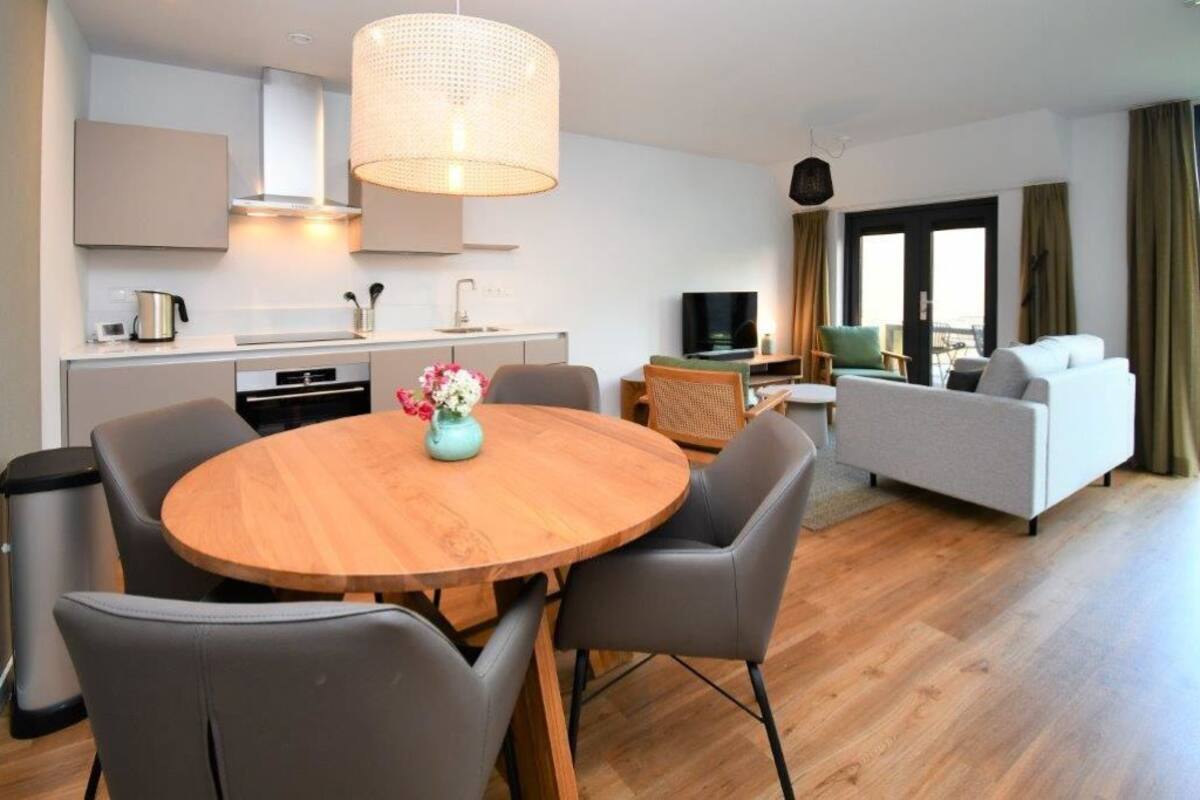 Una sala de estar moderna con una mesa redonda de madera, sillas grises, un sofá y una televisión.