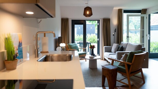 A modern kitchen with a sink, a dining area with a table and chairs, and a seating area with a sofa and chairs. - Skylgerduin (Midsland)
