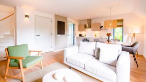 A modern living room with a white sofa, a green chair, and a dining area with a table and chairs. - Skylgerduin (Midsland)