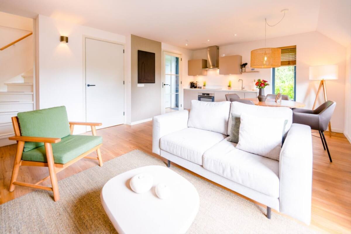 Una sala de estar moderna con un sofá blanco, un sillón verde y un comedor con mesa y sillas.