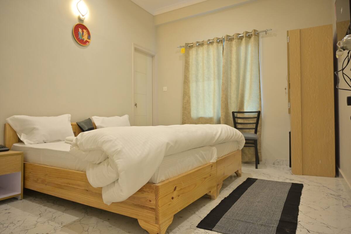 A bedroom with a wooden bed, a nightstand, a chair, a wardrobe, and a window with curtains.