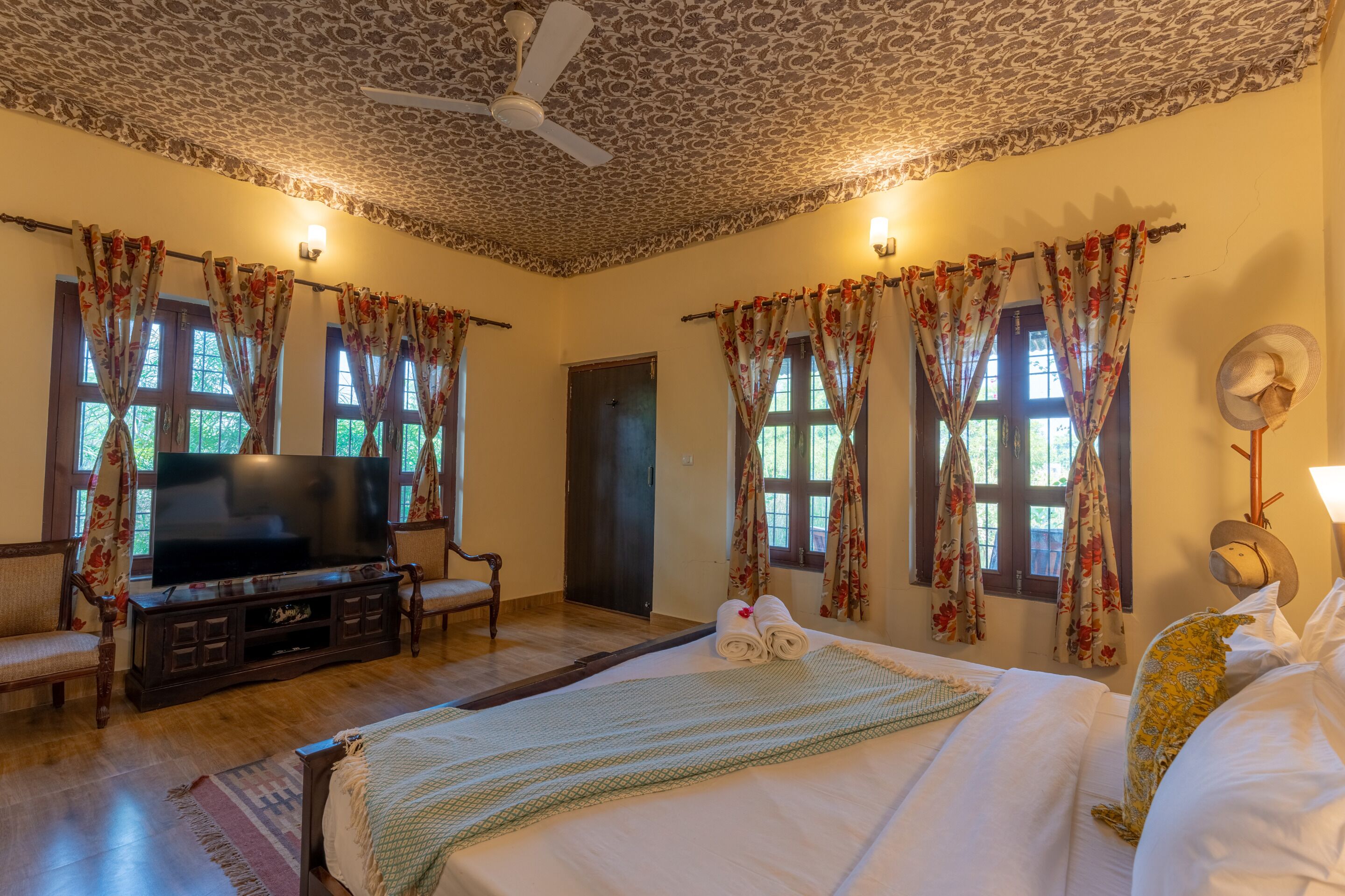 A room with a bed, a television, a ceiling fan, and floral curtains.
