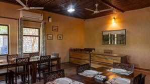Uma sala de jantar com uma mesa de madeira posta para seis pessoas, rodeada por cadeiras com detalhes elaborados nas costas.
