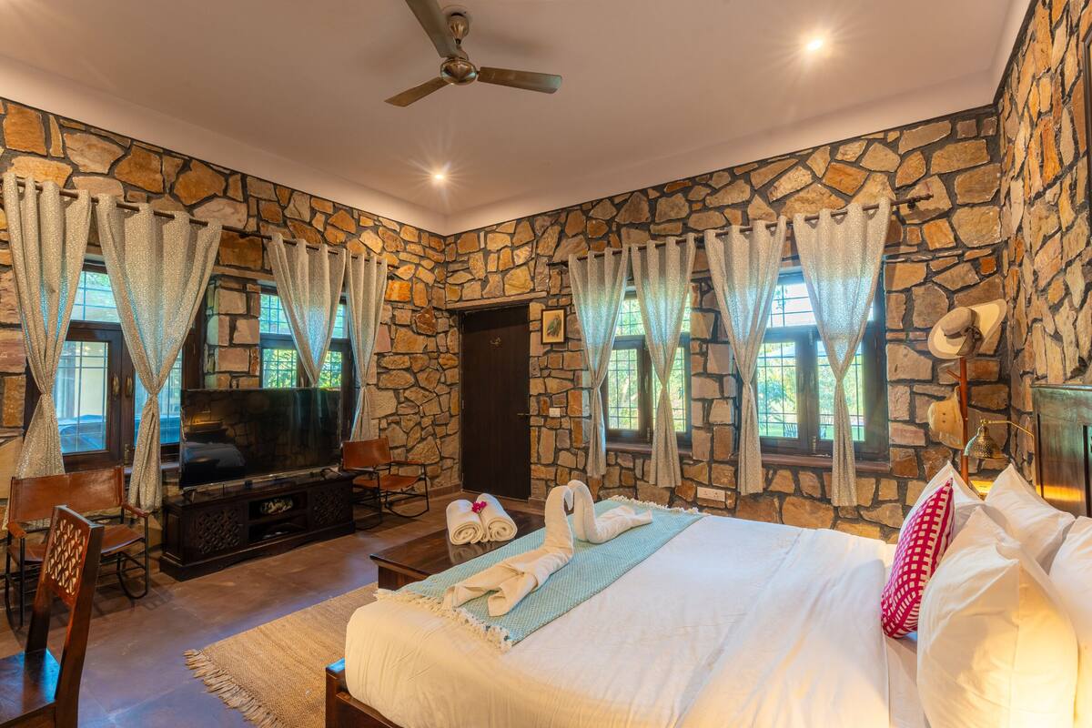 A bedroom with stone walls, a bed, a TV, and a ceiling fan.