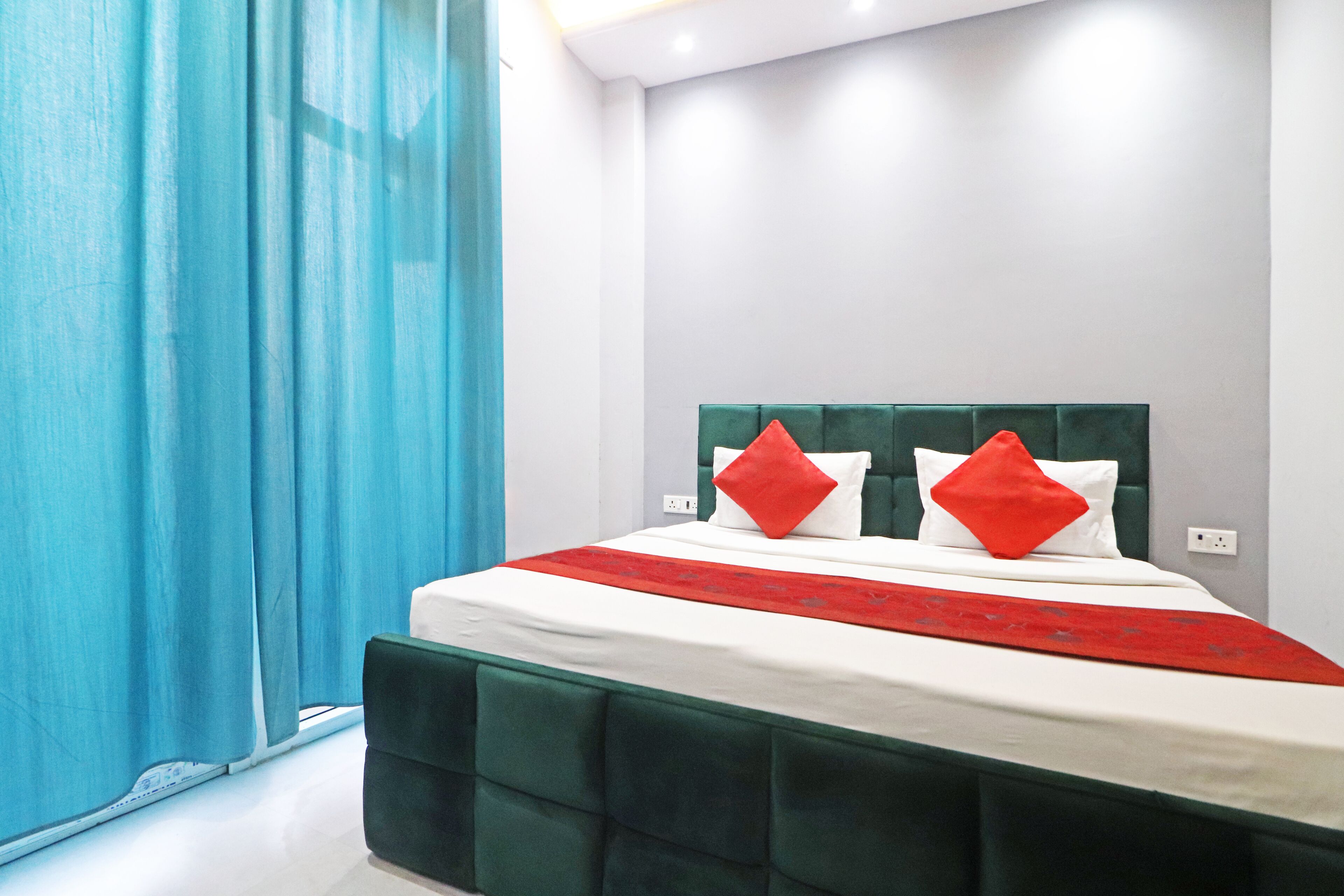 A neatly made bed with a green headboard and red pillows, a white bedspread, and a red runner.