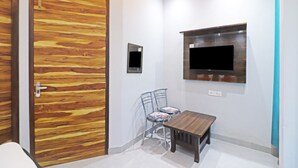 A room with a wooden door, a small table, two chairs, a wall-mounted TV, and a power outlet. - Twamev Rajouri garden by The Arrow (New Delhi)